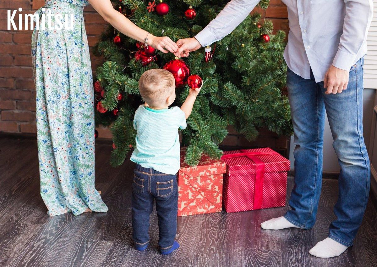 Une famille souriante décorant ensemble un sapin de Noël dans un salon chaleureux et lumineux.