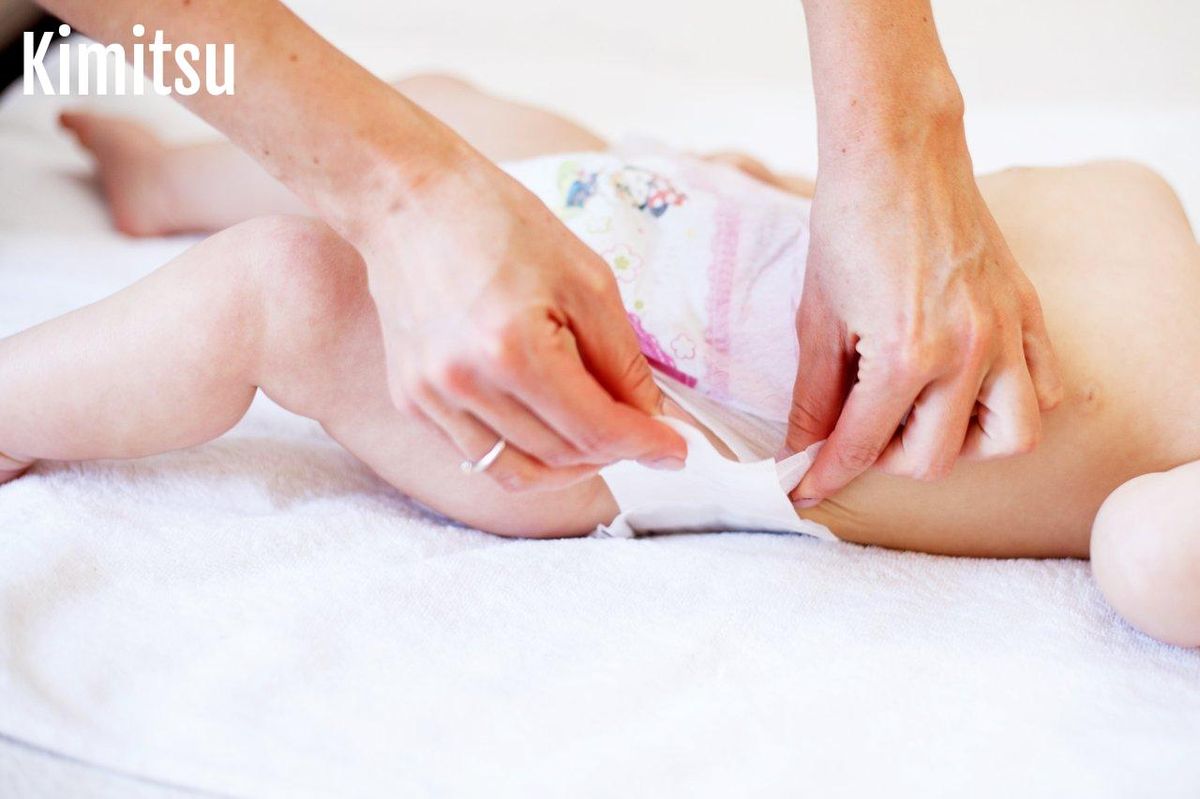 Une installation précise d'une couche bébé, mettant en valeur l'ajustement des élastiques des cuisses et du dos.