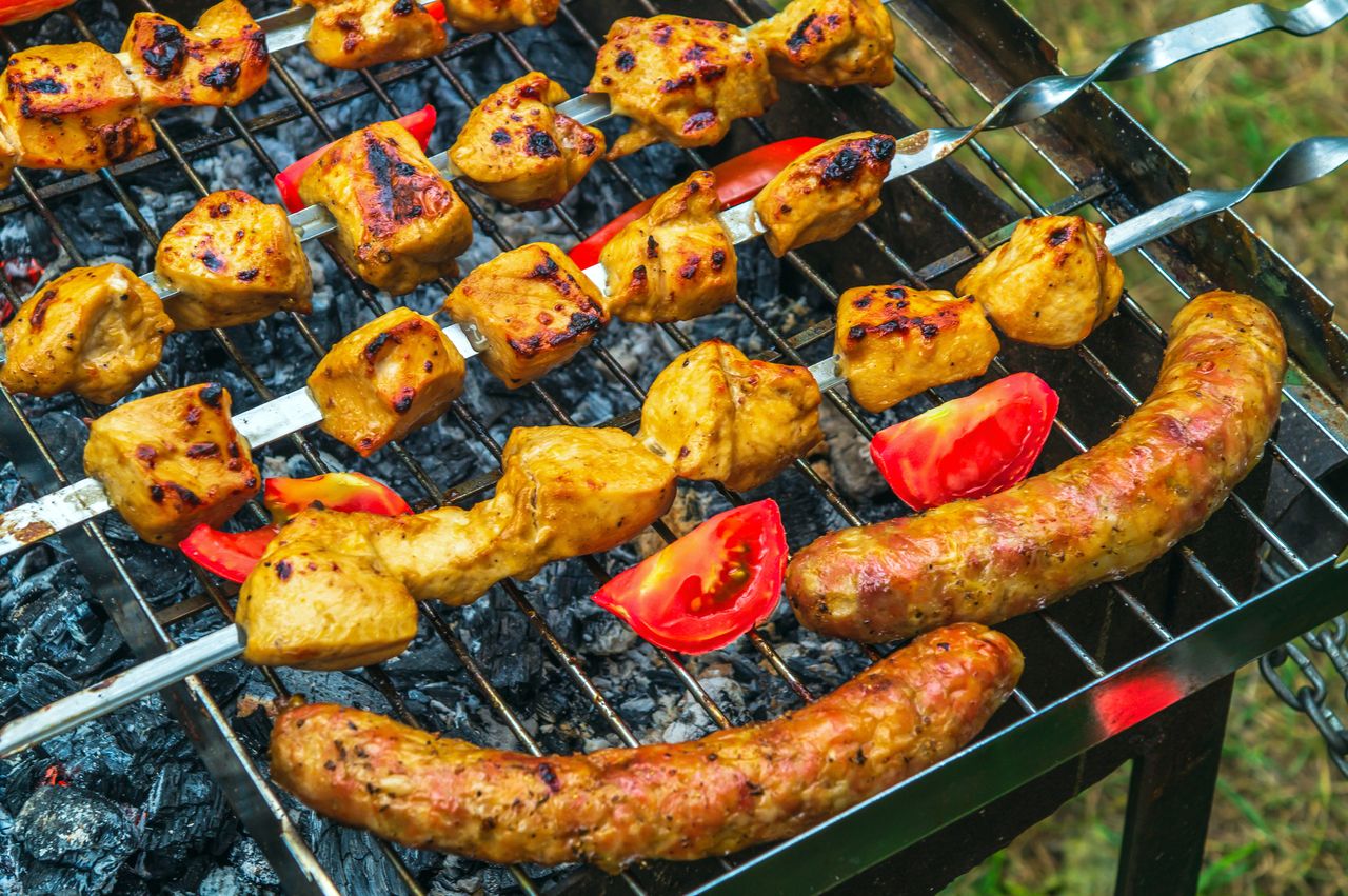 Barbecue au charbon avec braises, viande, légumes et fruits grillés, idéal pour une cuisson estivale savoureuse.