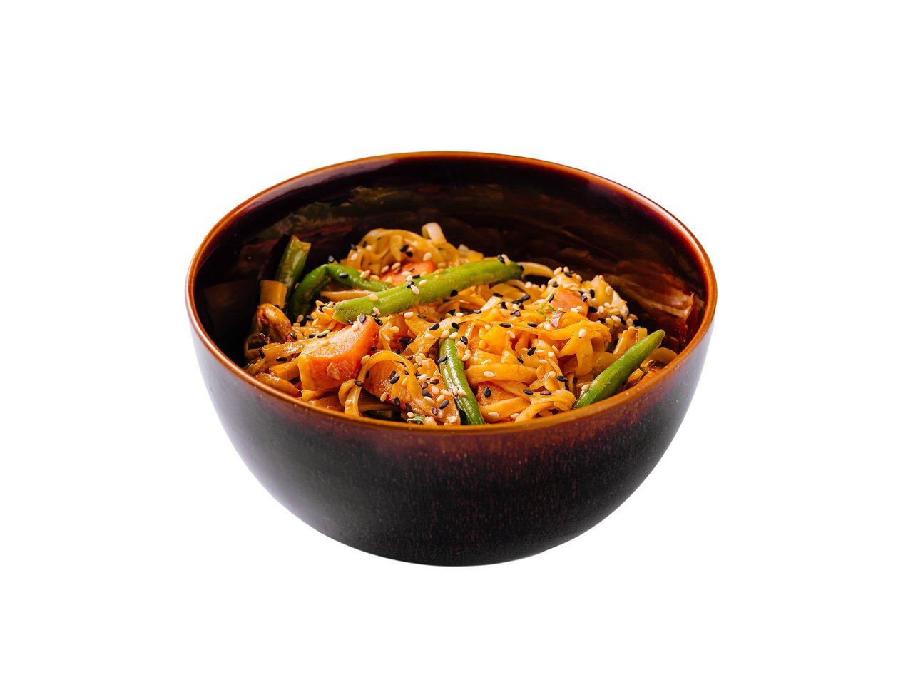 Bol de asian noodles chili crisp avec légumes, herbes fraîches et sauce savoureuse sur plan de travail en bois.