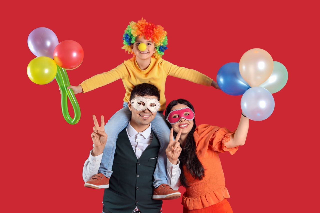 Enfant émerveillé devant une scène de théâtre colorée, entouré de sa famille en costumes et ballons.