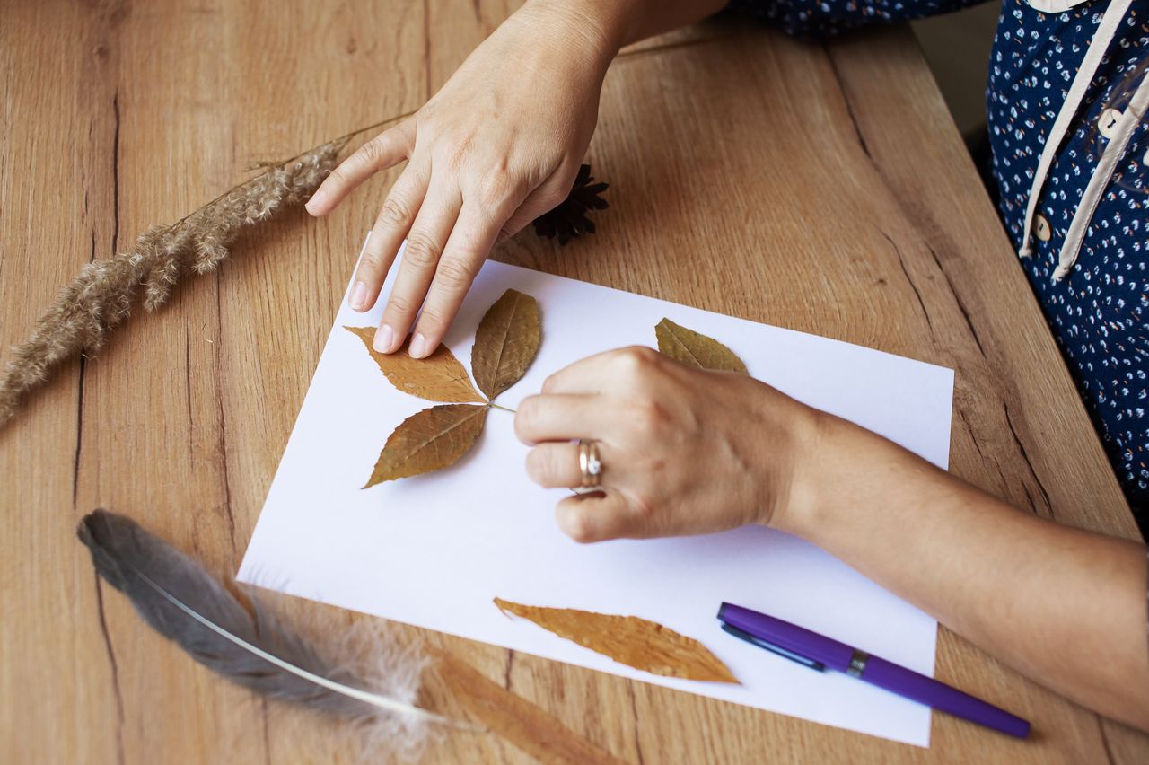 Enfants créant un bricolage d’automne avec feuilles, marrons et pommes de pin sur table claire.
