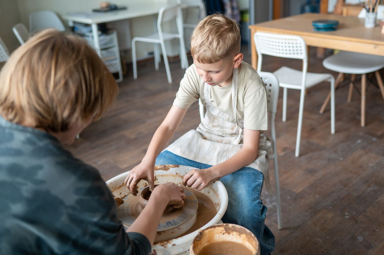 Enfants en atelier créatif d’été, apprenant la poterie avec argile, pinceaux et papier.