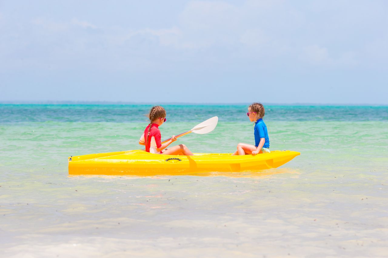 Enfants en colonie de vacances sur un plan d’eau, kayak, voile et ambiance estivale joyeuse.