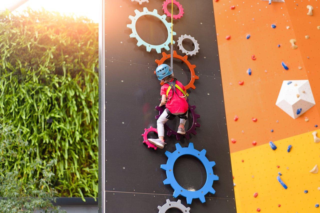 Enfants souriants avec un moniteur sur un mur d'escalade en salle, utilisant des prises colorées pour une activité sécurisée.