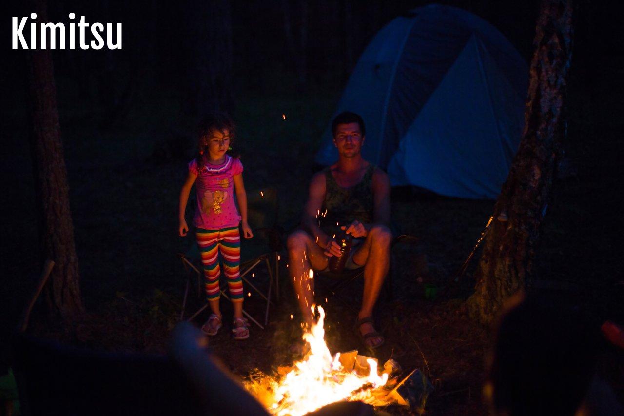 Famille profitant d’un camping au bord du lac avec feu de camp convivial en pleine nature.