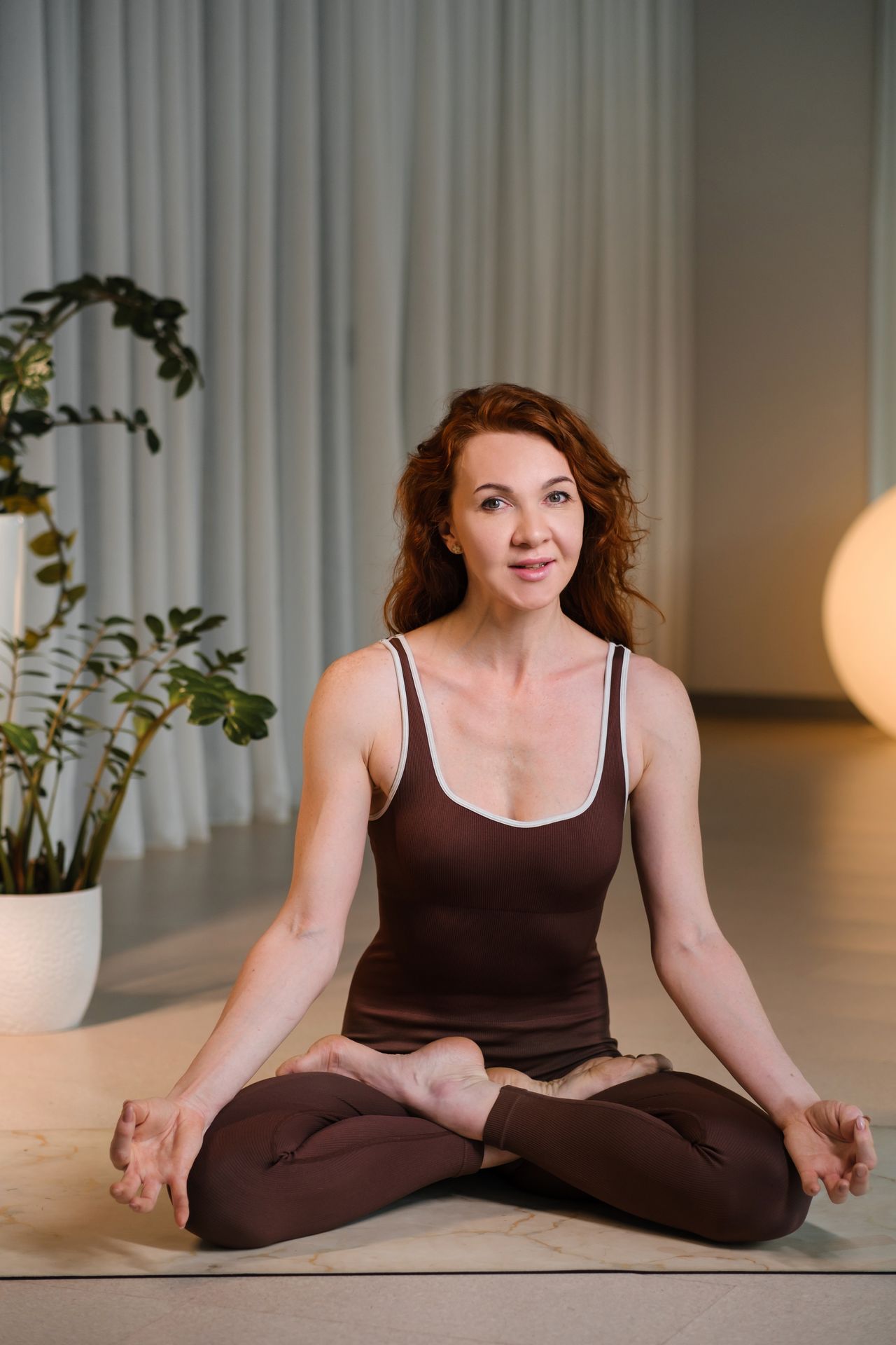Femme pratiquant un yoga doux à la maison, baignée de lumière naturelle et entourée de plantes.