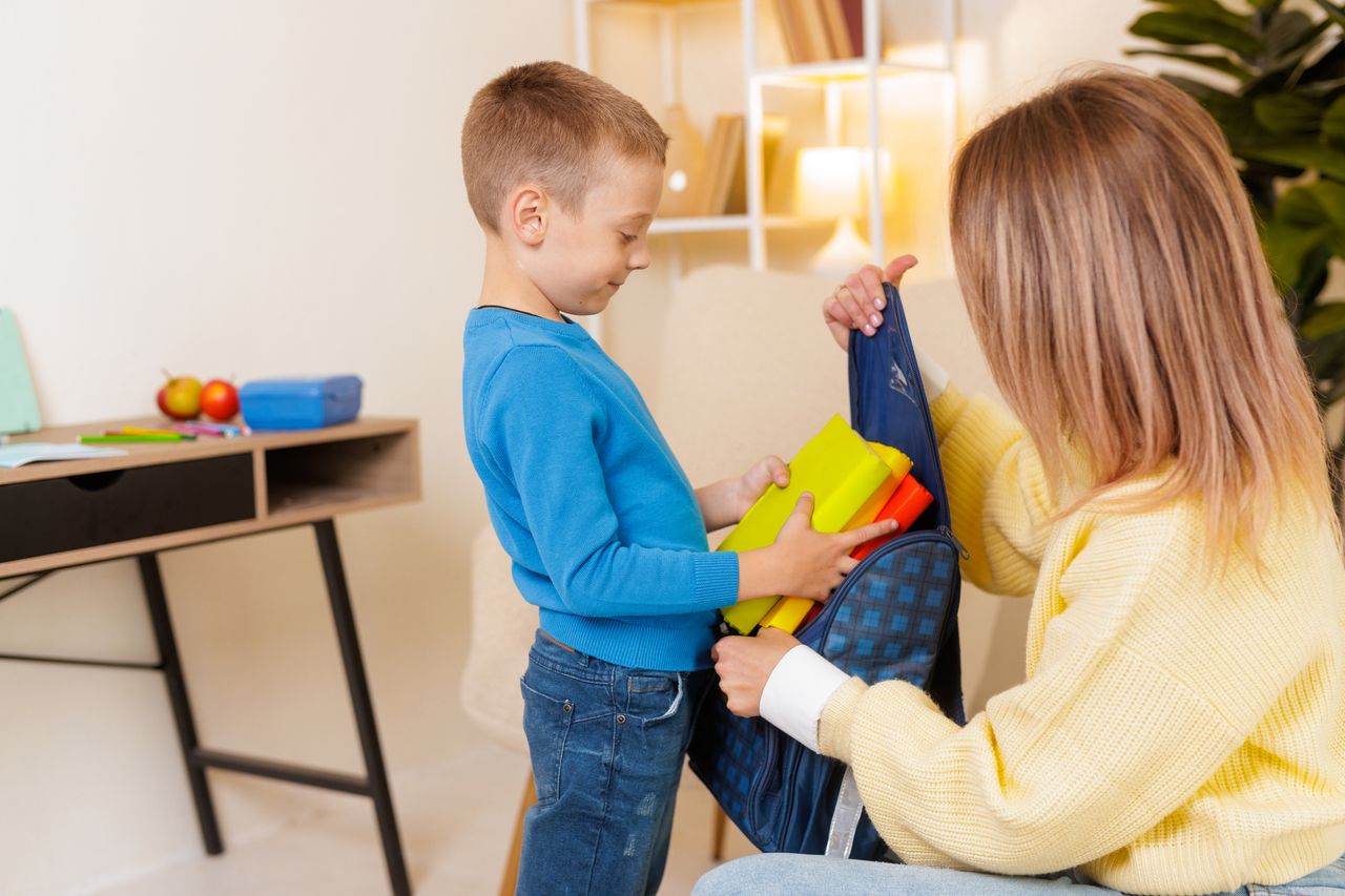 Mère aide son fils à préparer son sac d'école avec livres et fournitures à la maison.