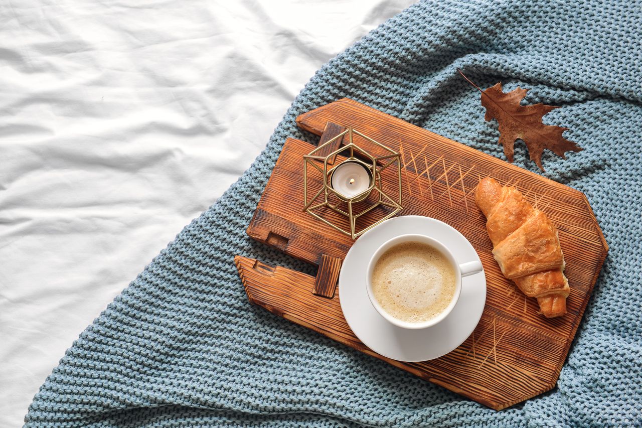 Quatre flacons d’huiles essentielles sur un plaid en laine, avec branche de sapin et tasse chaude.
