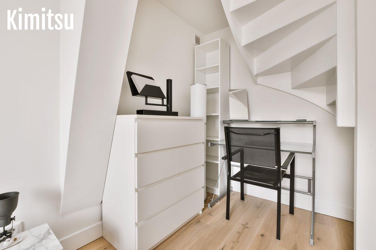 Espace de travail pour enfants sous l'escalier avec bureau blanc, chaise et rangements intégrés.